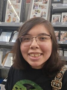 A smiling young person wearing glasses and a black shirt, standing in front of a store display with various photo frames
