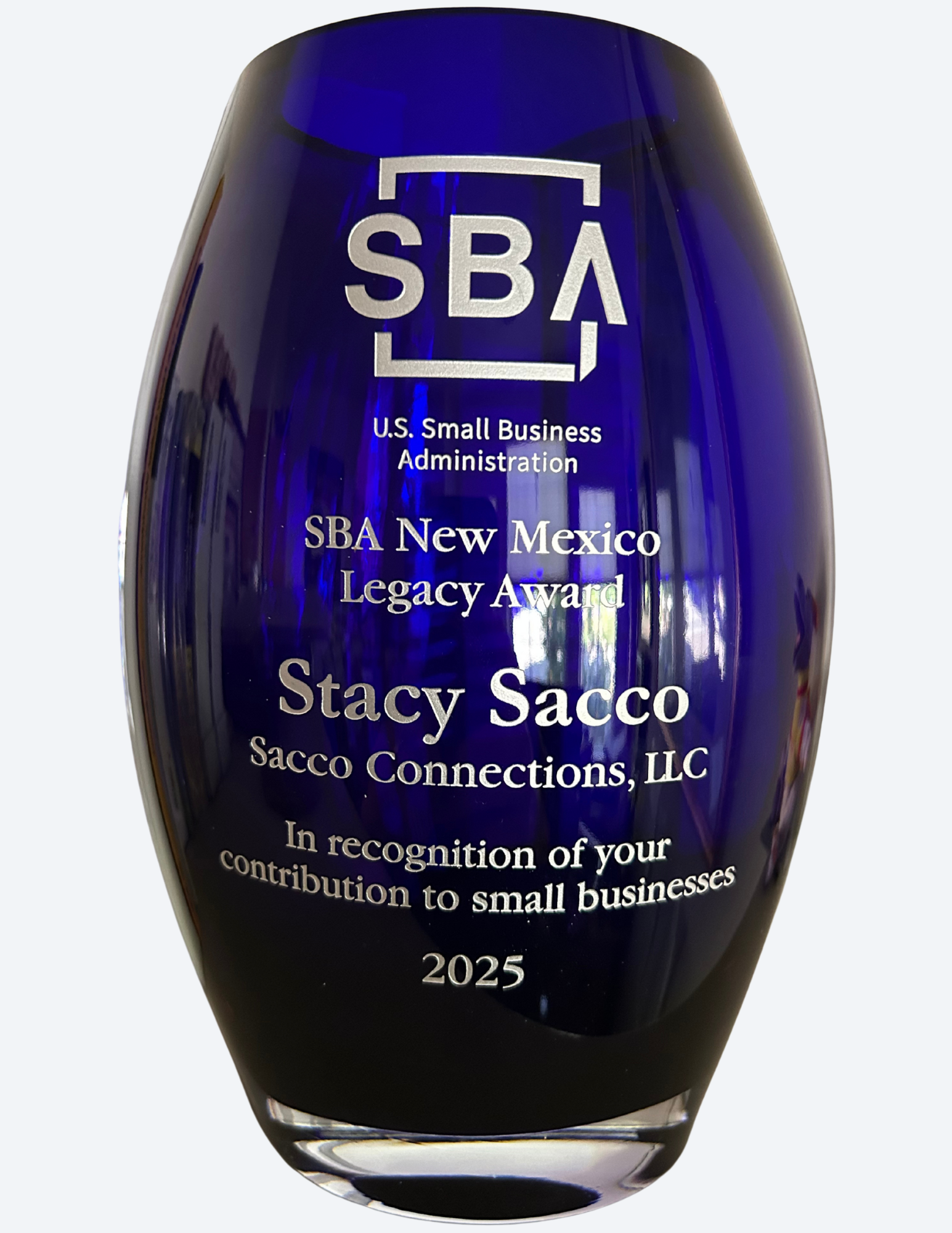 A deep blue glass award from the U.S. Small Business Administration, labeled 'SBA New Mexico Legacy Award,' presented to Stacy Sacco of Sacco Connections, LLC, in 2025, honoring contributions to small businesses