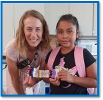 An woman with light brown hair in a pink shirt standing next to a young girl with brown hair pulled back into a ponytail while wearing a pink backpack.