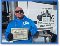 Man in a blue hoodie and sunglasses holding a certificate in front of a commercial truck with a company logo.